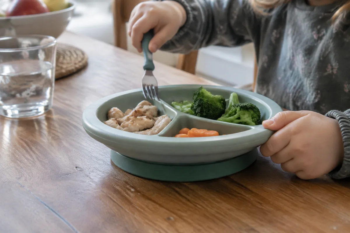 Assiette enfant stable avec rebord accessible et couverts sur une table familiale
